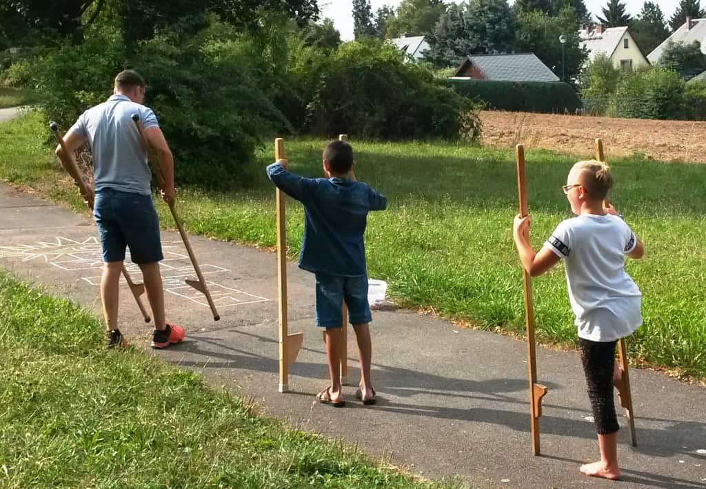 1 Erwachsener und 2 Kinder mit Stelzen